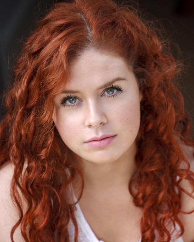 A woman with curly red hair and green eyes looking directly at the camera participates in role play training.