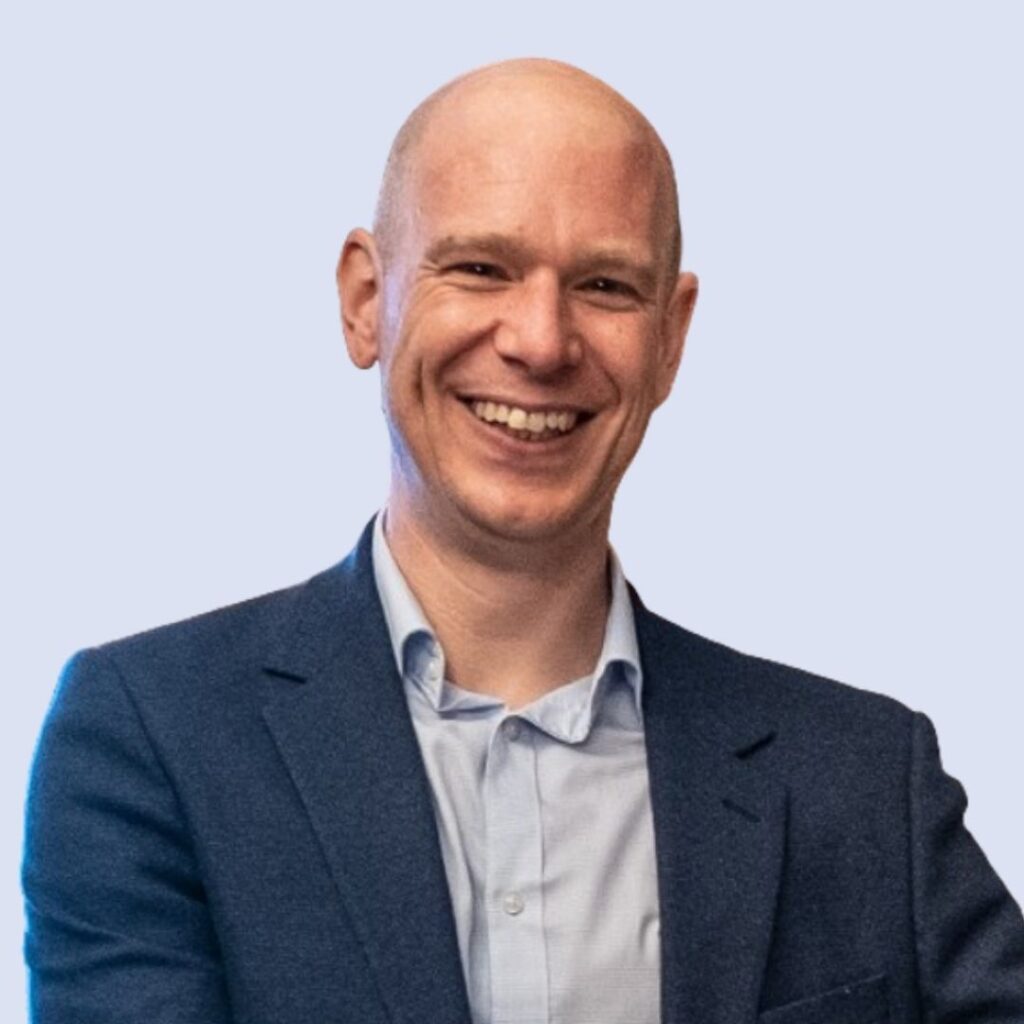 A person in a suit smiles at the camera with a neutral background.